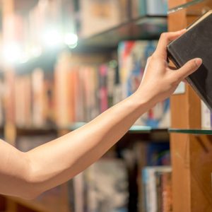 Right hand of young man picking a book from bookshelf in library, reading and learning concepts
