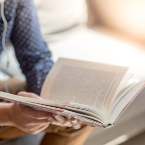 Young Asian man university student reading book on sofa in library, education research and self learning in university life concepts